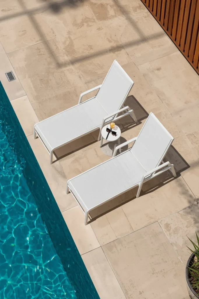 24 Outdoor Patio Furniture Ideas That Are Stylish, Comfy & Weather-Ready 17 poolside patio, featuring two white powder-coated aluminum chaise lounges