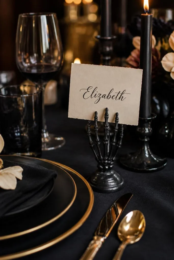 18 Elegant Halloween Dining Table Ideas for a Chic Fright Night 11 place setting close-up, featuring a matte black skeleton hand prop holding an upright calligraphy