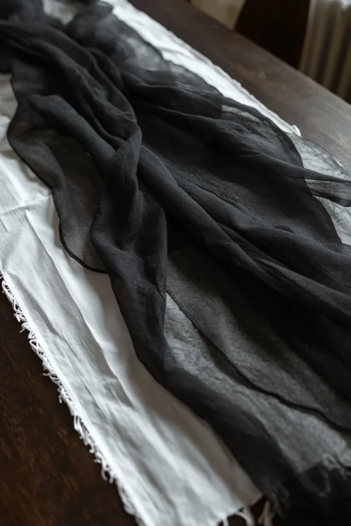 18 Elegant Halloween Dining Table Ideas for a Chic Fright Night 3 table runner close-up, featuring black gauzy creepy cloth draped unevenly over a white linen tablecloth